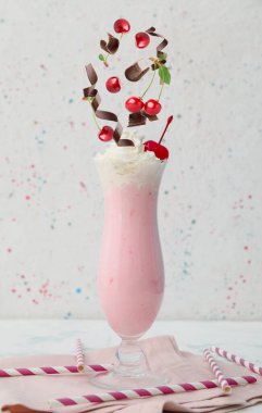 Beyaz arka planda bir bardak lezzetli milkshake ve dökülen malzemeler.