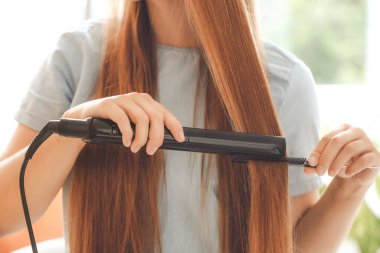 Güzel genç bayan evde saç için ütü kullanıyor.