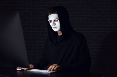Profesyonel hacker karanlık odadaki masada bilgisayar üzerinde çalışıyor.