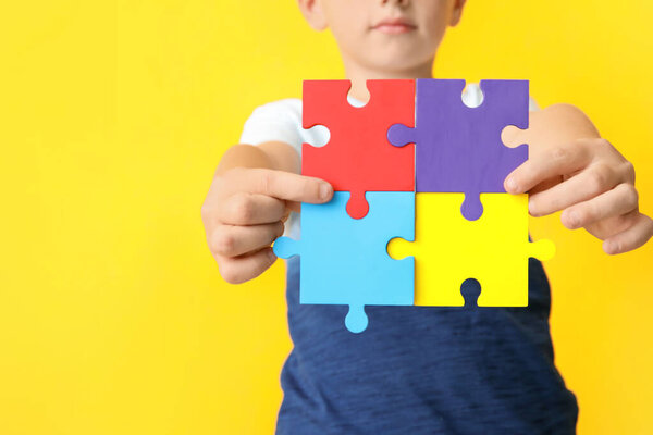 Little boy with autistic disorder doing puzzle on color background