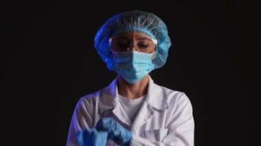 Olgun kadın doktor koyu arka planda koruyucu eldivenler giyiyor.