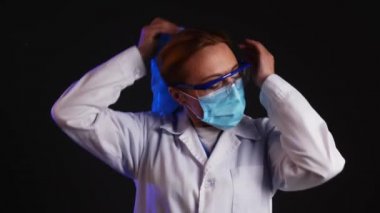 Yorgun kadın doktor koruyucu şapkasını, gözlüklerini ve maskesini çıkarıyor.