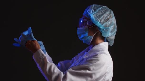 Reife Ärztin Zieht Medizinische Schutzhandschuhe Bevor Sie Vor Dunklem Hintergrund — Stockvideo