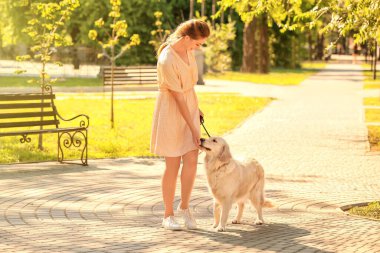 Parkta yürüyen sevimli köpekli genç bir kadın.