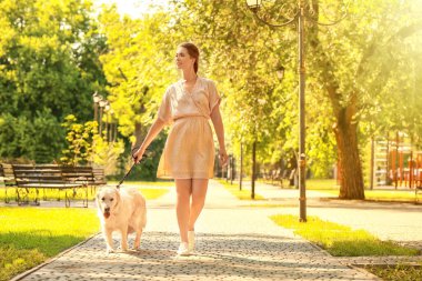 Parkta yürüyen sevimli köpekli genç bir kadın.