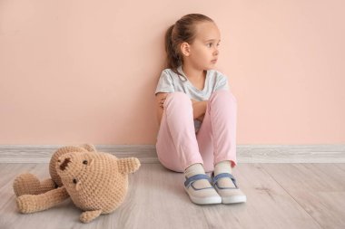 Otistik bozukluğu ve oyuncağı olan üzgün küçük kız renk duvarının yanında oturuyor.