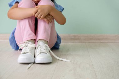Otistik bozukluğu olan küçük kız renk duvarının yanında oturuyor.