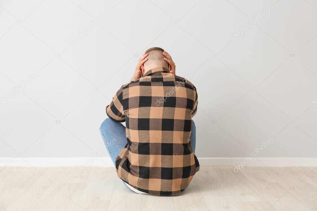 Depressed man sitting on floor near light wall