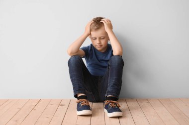 Otistik bozukluğu olan üzgün küçük çocuk ışık duvarının yanında oturuyor.