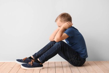 Otistik bozukluğu olan üzgün küçük çocuk ışık duvarının yanında oturuyor.