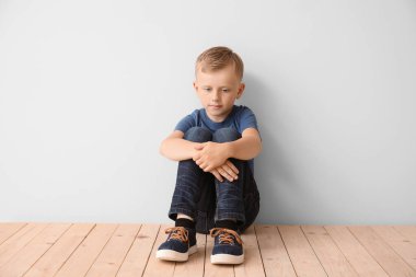 Otistik bozukluğu olan üzgün küçük çocuk ışık duvarının yanında oturuyor.