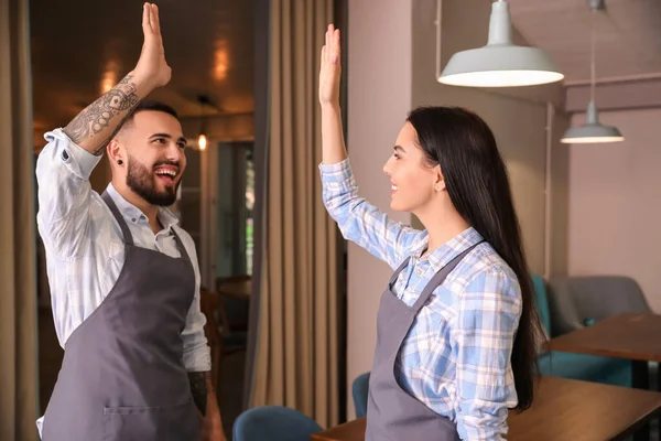 Young waiters giving high-five to each other in restaurant