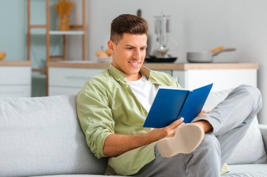 Kitaplı genç adam evdeki koltukta dinleniyor.
