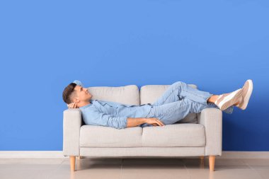 Genç adam renk duvarının yanındaki kanepede dinleniyor.