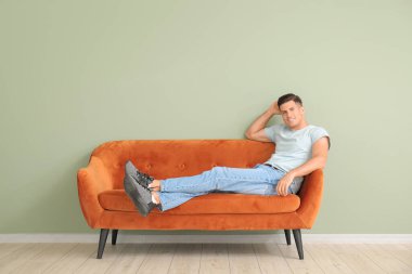 Genç adam renk duvarının yanındaki kanepede dinleniyor.