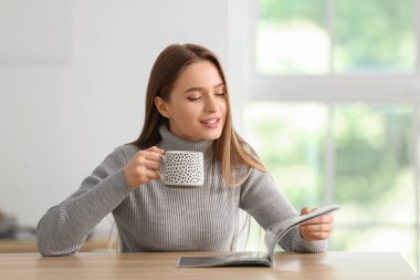 Evde çay içip dergi okuyan güzel genç bir kadın.