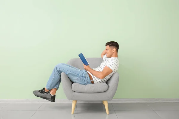 Joven Hombre Leyendo Libro Mientras Relaja Sillón Cerca Pared Color —  Fotos de Stock