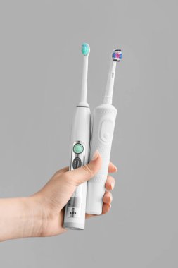 Gri arka planda elektrikli diş fırçaları olan bir el.