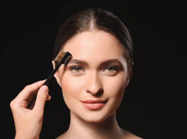Siyah arka planda makyaj yapan genç bir kadın.
