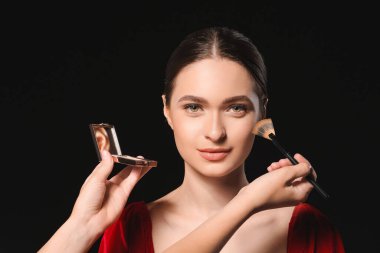 Makyaj sanatçısı karanlık arka planda genç ve güzel bir kadınla çalışıyor.