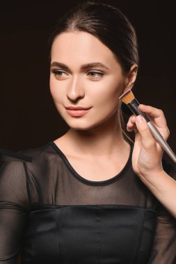 Makyaj sanatçısı karanlık arka planda genç ve güzel bir kadınla çalışıyor.