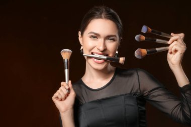 Siyah arka planda makyaj fırçası olan genç bir kadın.