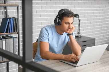 Ofiste çalışan kulaklıklı ve laptoplu bir adam.
