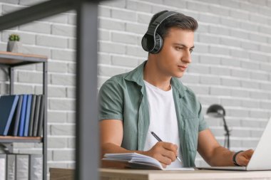 Ofiste çalışan kulaklıklı ve laptoplu bir adam.