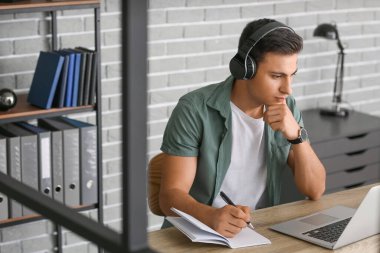 Ofiste çalışan kulaklıklı ve laptoplu bir adam.