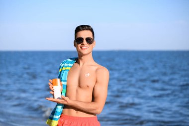 Deniz sahilinde güneş kremi sürmüş yakışıklı bir genç.
