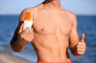 Deniz sahilinde güneş kremi sürmüş yakışıklı genç adam, yakın plan.