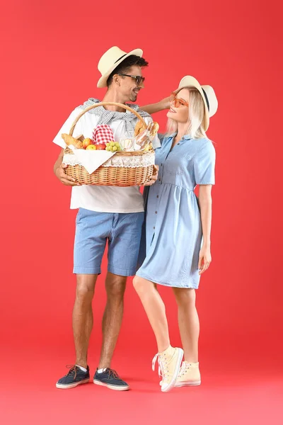 Young couple with food for picnic in basket on color background