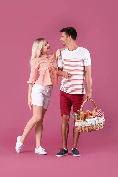 Young couple with food for picnic in basket on color background