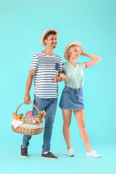 Young couple with food for picnic in basket on color background