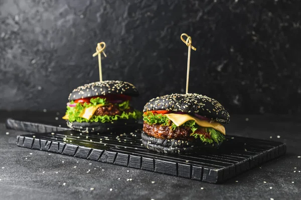 Tasty burgers with black bun on dark background