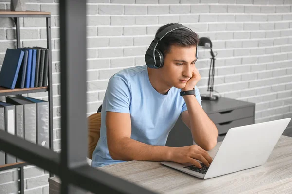 Ofiste çalışan kulaklıklı ve laptoplu bir adam.