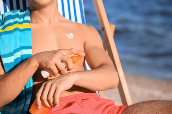 Handsome young man applying sunscreen cream on sea beach