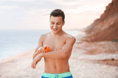 Deniz sahilinde güneş kremi süren yakışıklı genç adam.