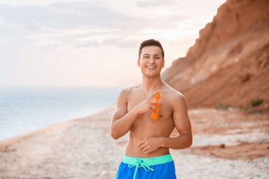 Deniz sahilinde güneş kremi sürmüş yakışıklı bir genç.