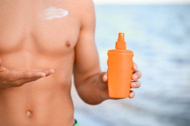 Deniz sahilinde güneş kremi sürmüş yakışıklı genç adam, yakın plan.