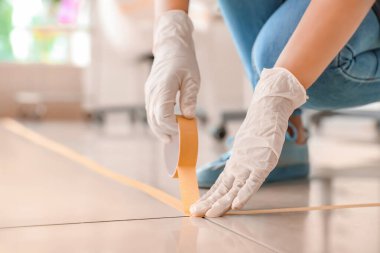 Kadın makyaj sanatçısı Coronavirus salgını sırasında salonda yere bant yapıştırıyor.