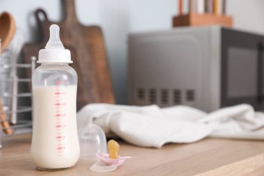 Bebek için bir şişe süt, emzik ve giysi.