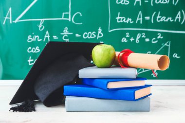 Mezuniyet şapkası, kitaplar, elma ve diploma sınıftaki masada.