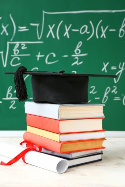 Mezuniyet şapkası, kitaplar ve diploma sınıftaki masada.