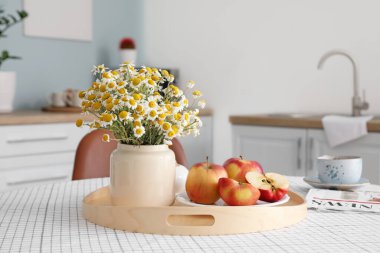 Modern mutfağın içinde, yemek masasında çiçekli ve elmalı vazo.