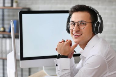 Ofiste çalışan kulaklıklı ve bilgisayarlı bir adam.