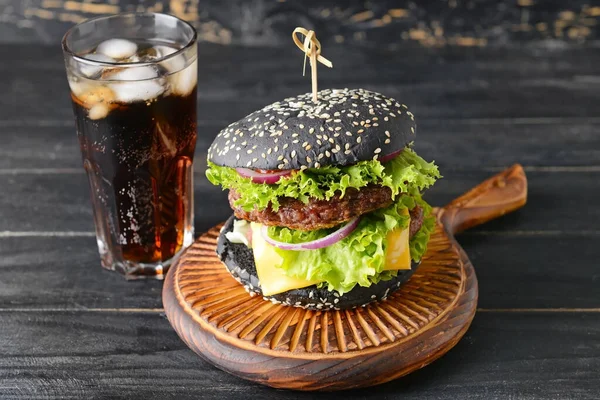 Tasty burger with black bun and cola drink on table