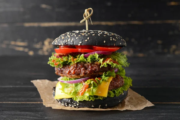 Tasty burger with black bun on dark background