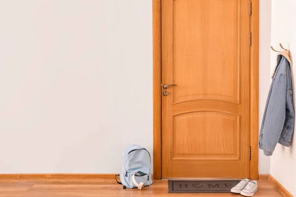 Door mat with backpack and shoes on floor in hallway