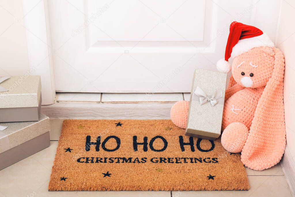 Door mat with toy and Christmas gifts on floor in hallway